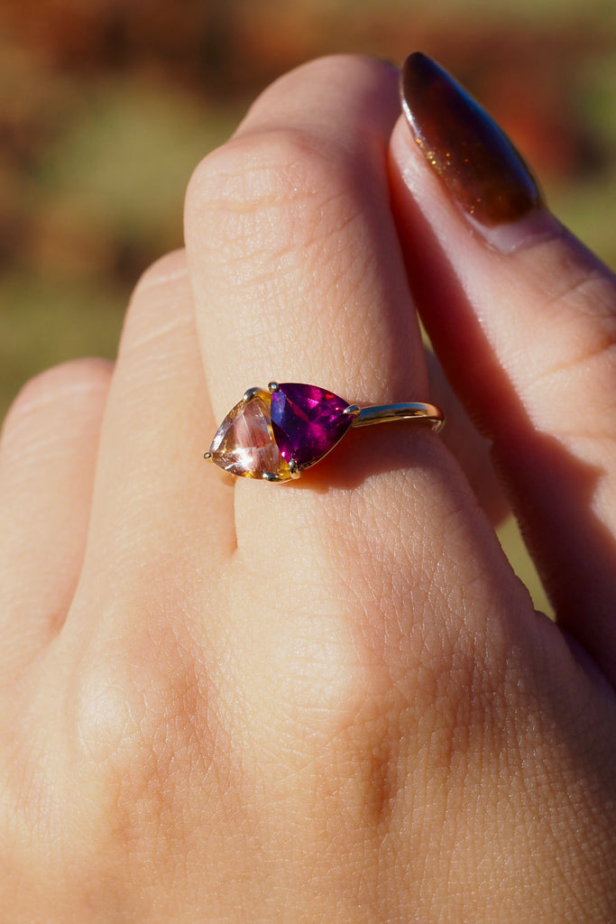 ジュエリースタジオMASHIROのアップサイクルジュエリー。オレゴンサンストーン・トリリアントカット・約1.07ct・約6.8*6.6mm・アメリカオレゴン州産｜ロードライトガーネット・トリリアント・約1.17ct・約7mm・インド産。シャンパンゴールドカラーのコンビリングの着用画像。