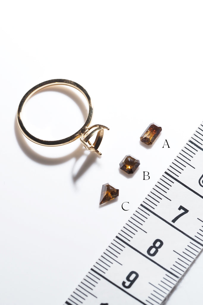オンラインジュエリースタジオMASHIROカラーダイヤモンド・キャラメルサンセット3石とリングの空枠をメジャーの横に並べた写真
