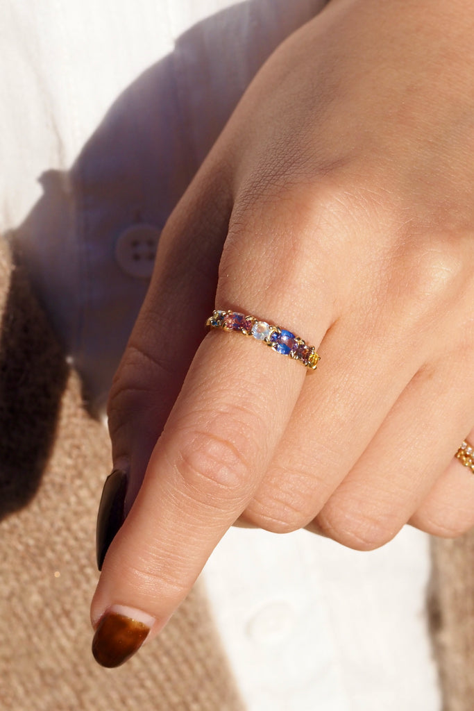 ジュエリースタジオMASHIROのアップサイクルジュエリー。マラヤガーネット・オーバル・約0.3ct・約 5*3mm・タンザニア産｜タンザナイト・オーバルカット・約0.28ct・約4.9*3.8mm｜レインボーームーンストーン・ラウンド・約0.09ct・約3mm｜マルチカラーサファイア（３石：ラウンド・プリンセス・ヘキサゴン）・合計：0.34ct・約2.6mm。シャンパンゴールドカラーのカクテルエタニティリングの着用画像。