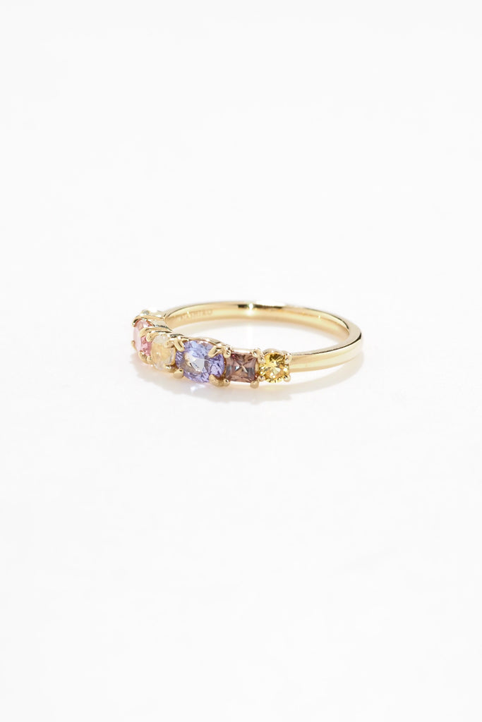 ジュエリースタジオMASHIROのアップサイクルジュエリー。マラヤガーネット・オーバル・約0.3ct・約 5*3mm・タンザニア産｜タンザナイト・オーバルカット・約0.28ct・約4.9*3.8mm｜レインボーームーンストーン・ラウンド・約0.09ct・約3mm｜マルチカラーサファイア（３石：ラウンド・プリンセス・ヘキサゴン）・合計：0.34ct・約2.6mm。シャンパンゴールドカラーのカクテルエタニティリング。