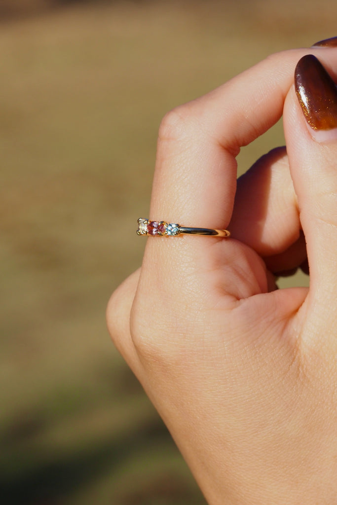 ジュエリースタジオMASHIROのアップサイクルジュエリー。マラヤガーネット・オーバル・約0.3ct・約 5*3mm・タンザニア産｜タンザナイト・オーバルカット・約0.28ct・約4.9*3.8mm｜レインボーームーンストーン・ラウンド・約0.09ct・約3mm｜マルチカラーサファイア（３石：ラウンド・プリンセス・ヘキサゴン）・合計：0.34ct・約2.6mm。シャンパンゴールドカラーのカクテルエタニティリング。